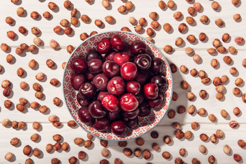 Top view of fresh sweet cherries in bowl with cherry seeds around on wooden table