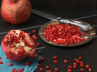 Half a fresh pomegranate on a blue napkin. Pomegranate grains on a plate and scattered on a black...