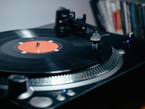 Closeup of top of old black turntable with tonearm maintaining position of cartridge tracing groove and playing LP record