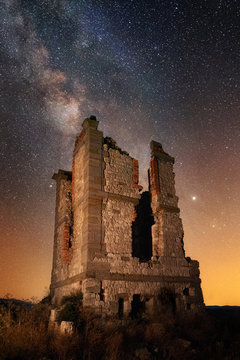 Dilapidated old brick tower on deserted field against majestic starry sky