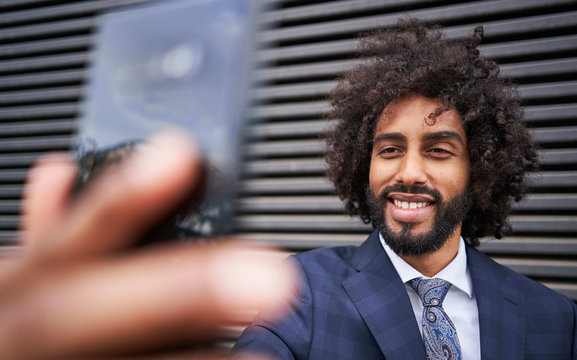 Bearded African American man with curly hair smiling while taking selfie next to striped wall