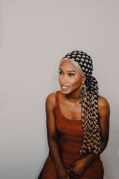 Beautiful adult African American female in brown dress patterned headscarf and earrings looking away on grey background