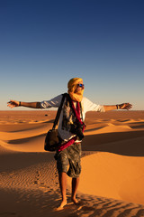 Unrecognizable tourist with outstretched arms standing against bright cloudless sundown sky in desert