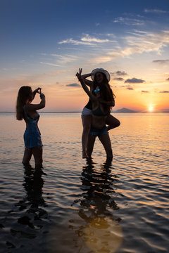 Happy girlfriends fooling and making photos at sunset at sea in summer
