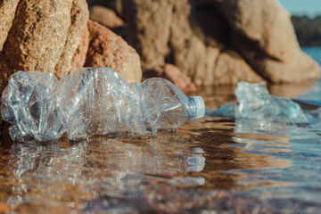 Empty plastic crumpled bottles waste lying in clear water on seaside near rocks