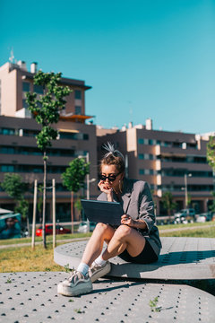 trendy businesswoman working outside sitting on round decorative panel plates nearby building in bright day