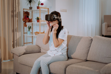 Amazed girl sitting on a gray sofa and looking in VR goggles