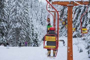 Skiers are sitting at old fashioned one chair ski lift.  Chair ski lift next to slope for skis and snowboards.  Ski area in snowy high mountain. Sports and recreation concept. Selective focus.