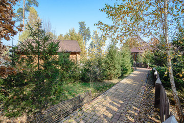 Fototapeta na wymiar The path along the wooden fence inside the recreation center. Golden autumn. Trees with yellow autumn leaves. Houses in the forest. Rest in wooden houses. Ukraine. v. Bobritsa. 10/20/2019