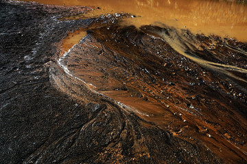 From above abstract dark ground with dirty puddle and dripping rusty water flows