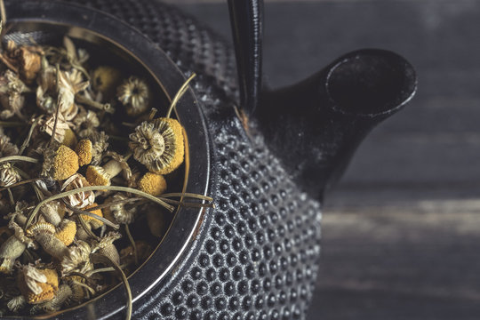 Closeup of dried daisy heap for tea making in metal teapot on dark table