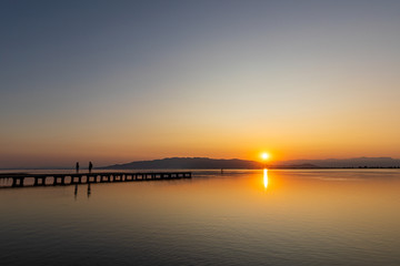 Romantic scene of a couple at sunset. Intense colors of a sunset with reflections in the water