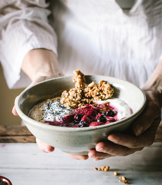 Crop person holding bowl with delicious crispy granola served with fresh berries yogurt and chia seeds