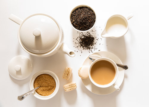 Traditional English Breakfast Black Tea With Milk -tea Leaves. Teacup, Teapot, Sugar And Milk Bowls, Macaroons Sweets On A White Background, Top View.