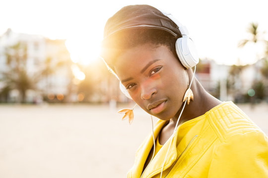 Portrait of African American woman in stylish bright jacket looking at camera on sandy beach blurred background