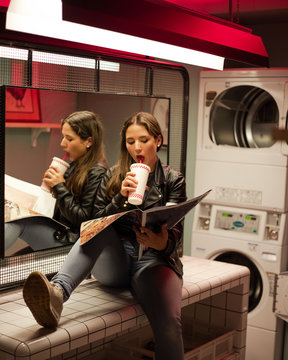 Carefree woman with drink and newspaper in modern laundromat