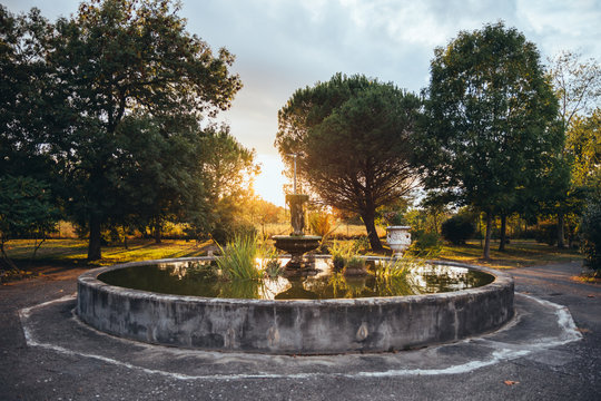 Aged stone round fountain in deserted park during golden sunset in summer time
