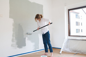 Woman rolling paint onto wall - Powered by Adobe
