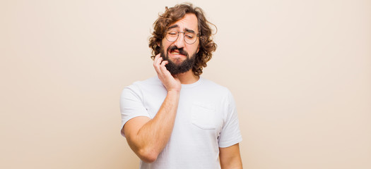 young bearded crazy man holding cheek and suffering painful toothache, feeling ill, miserable and...