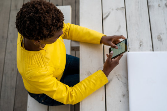 From above concentrated African American female messaging smartphone while relaxing at wooden table