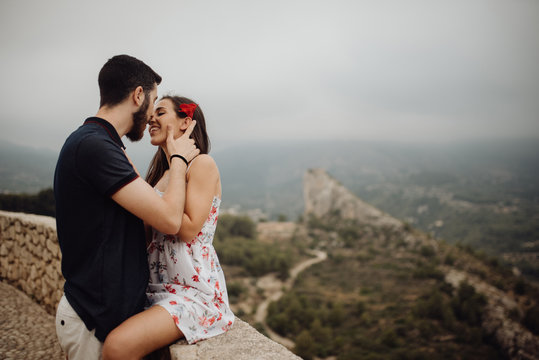 Side view of loving couple hugging and kissing while leaning on parapet of viewpoint at hazy mountain valley