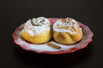 Two baked apples filled oats and powdered by sugar powder on red plate on black background