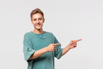 Handsome young man in a green tee showing with his fingers right at the empty space for advertising.