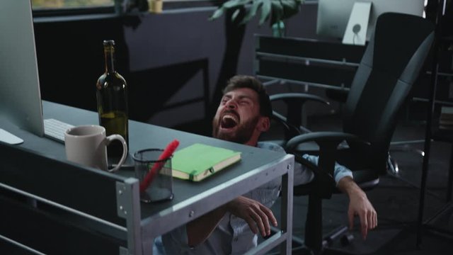 Fun office worker going crazy of alcohol lying on the floor and laughing hard. Drunk addicted business manager getting up sitting in chair. Alcohol intoxication.