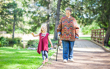 Smiling little girl walking in park with granny. Happy senior woman looking at her granddaughter at bridge