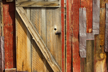 Old wooden door in disrepair with protruding nails and metal panels.