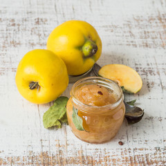 Homemade jam in glass jar and fresh fruit quince on an old table. Selective focus.