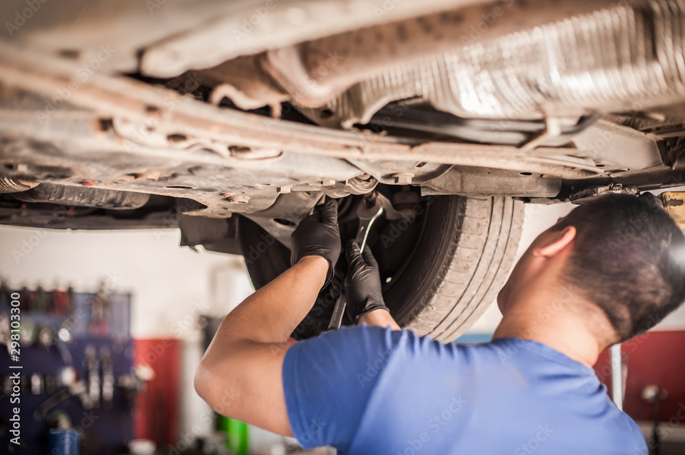 Wall mural auto mechanic repairer checking condition under car on vehicle lift