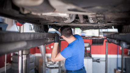 Auto mechanic repairer checking condition under car on vehicle lift