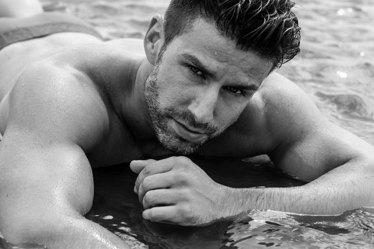 Handsome man with muscular body posing in the water in swimwear.