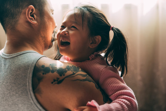 Father with tattoos playing with his daughter at home