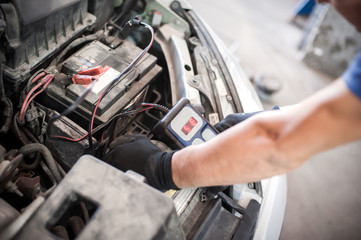 Fototapeta na wymiar Car mechanic checking and testing automotive accumulator with battery tester