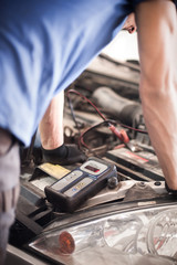 Obraz premium Car mechanic checking and testing automotive accumulator with battery tester