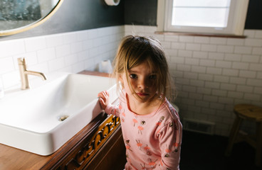 little girl gets ready in bathroom mirror