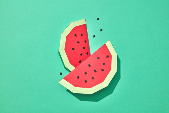 Two mouth-watering slices of red watermelon with seeds on a green background with space for text. Paper handcraft composition. Flat lay