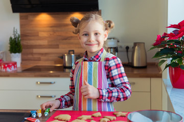 Portrait of pretty little girl with  funny pigtails decoraiting christmas cookies