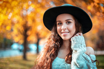 Pretty girl in hat standing on colorful autumn leaves background