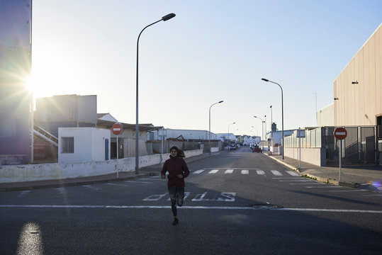Sportswoman running industrial zone sunrise.