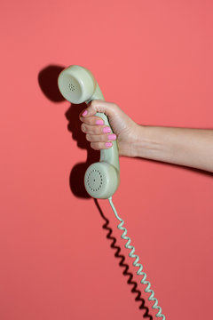 Hand holding a telephone in a coral background.