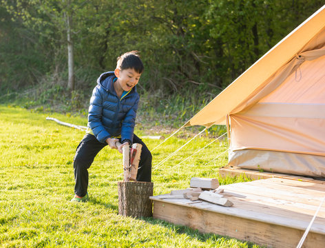 Boy cut wood with an axe under bright sunshine in campsite