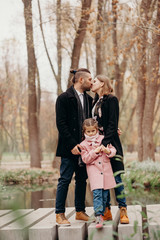Happy family. The father and mother embracing their daughter relaxing outdoors in autumn park