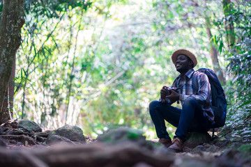 African freedom man traveler holding camera with backpack sitting in the green natural forest.