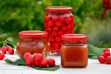 Jars of jam and compote of hawthorn on a wooden table on the background of the garden closeup