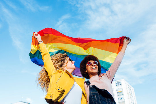 Two women friends hanging out in the city waving LGBT with pride flag