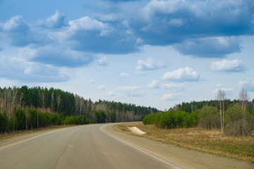 A long straight empty asphalt road through green forest on sunny day, perspective. Travel concept