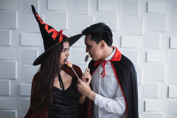 Asian young couple in costume witch and dracula on white wall.